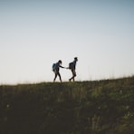 couple walking on hill while holding during daytime