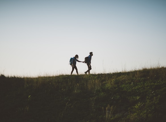 couple walking on hill while holding during daytime