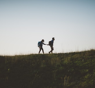 couple walking on hill while holding during daytime