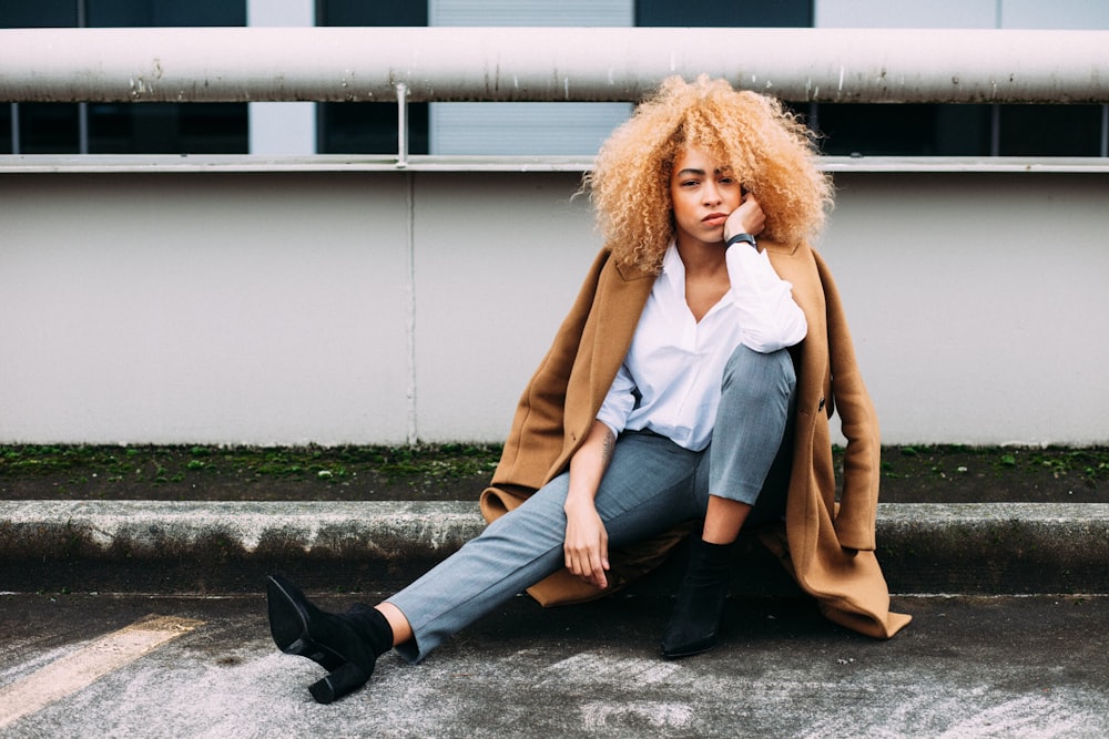 woman sitting on gray concrete pavement near white metal railing at daytime