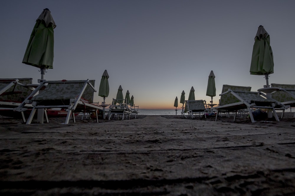 Photographie en contre-plongée de chaises longues avec des parasols à la plage au coucher du soleil