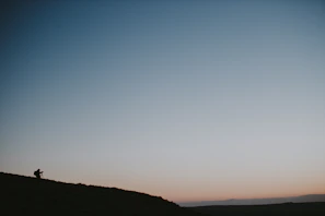 Wide shot of an Angolan landscape at dusk, with a lone figure filming.