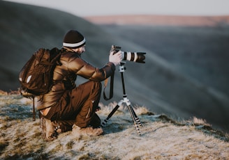 man taking photo using black and white DSLR camera on hill at daytime