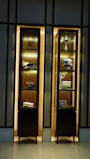 A pair of illuminated wooden display cabinets contain various items, including a decorative globe, a trophy, folded clothes, shoes, and framed pictures. The arrangement is neat and organized with some items showcasing luxury and elegance.