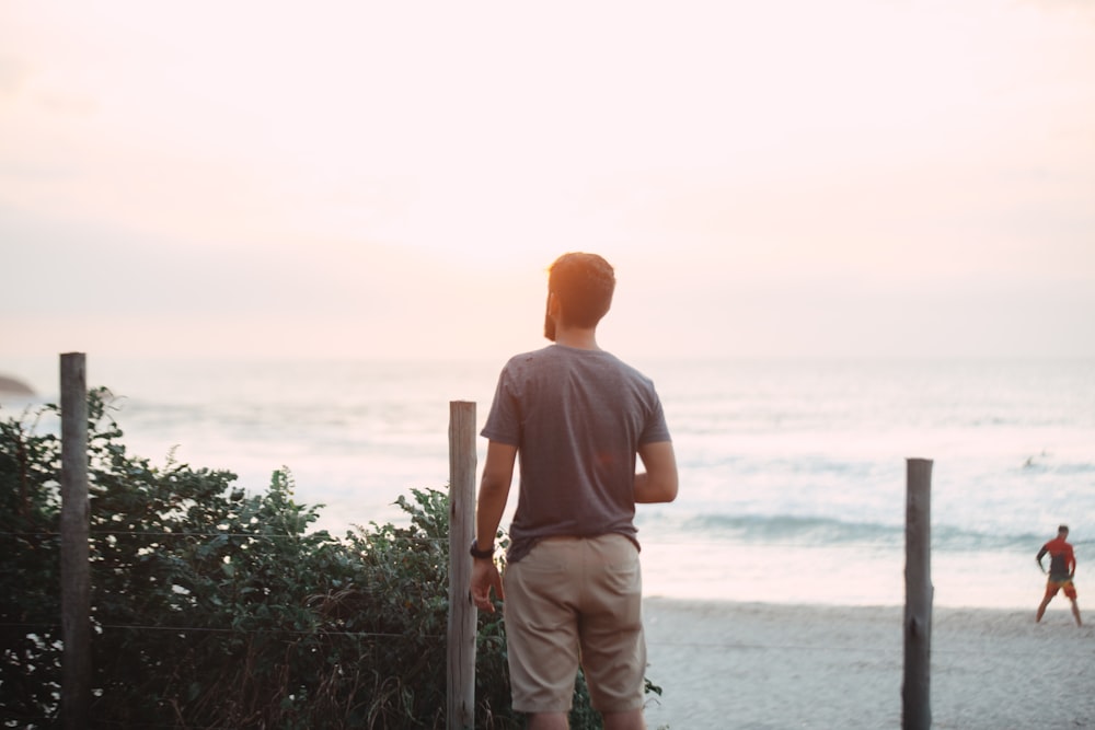 man standing near post facing beach