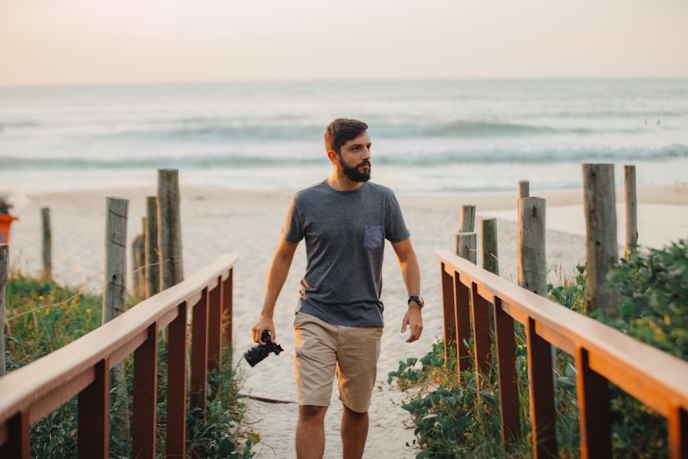 hombre caminando sosteniendo una cámara cerca de la costa