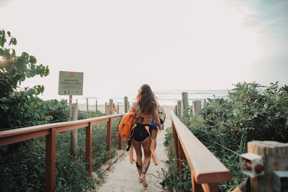 woman wearing pink and black bikini bringing orange surfboard