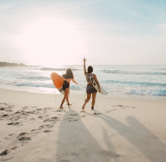 two women walking towards the ocean carrying surfboards during day