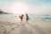 two women walking towards the ocean carrying surfboards during day