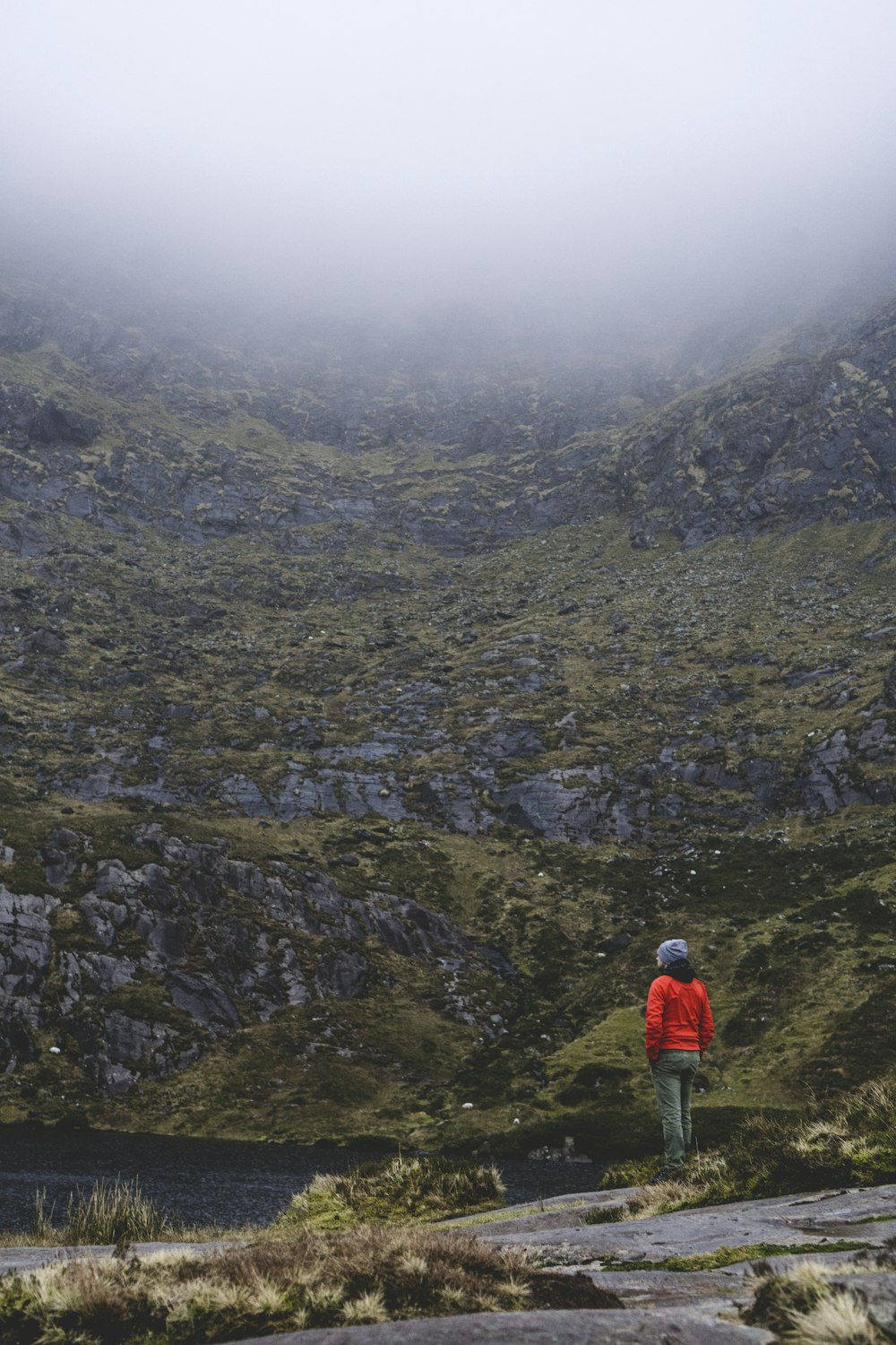 woman wearing orange jacket and blue knit hat facing the mountain