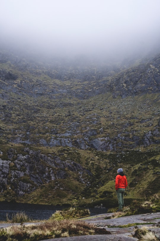 woman wearing orange jacket and blue knit hat facing the mountain in Conor Pass Ireland