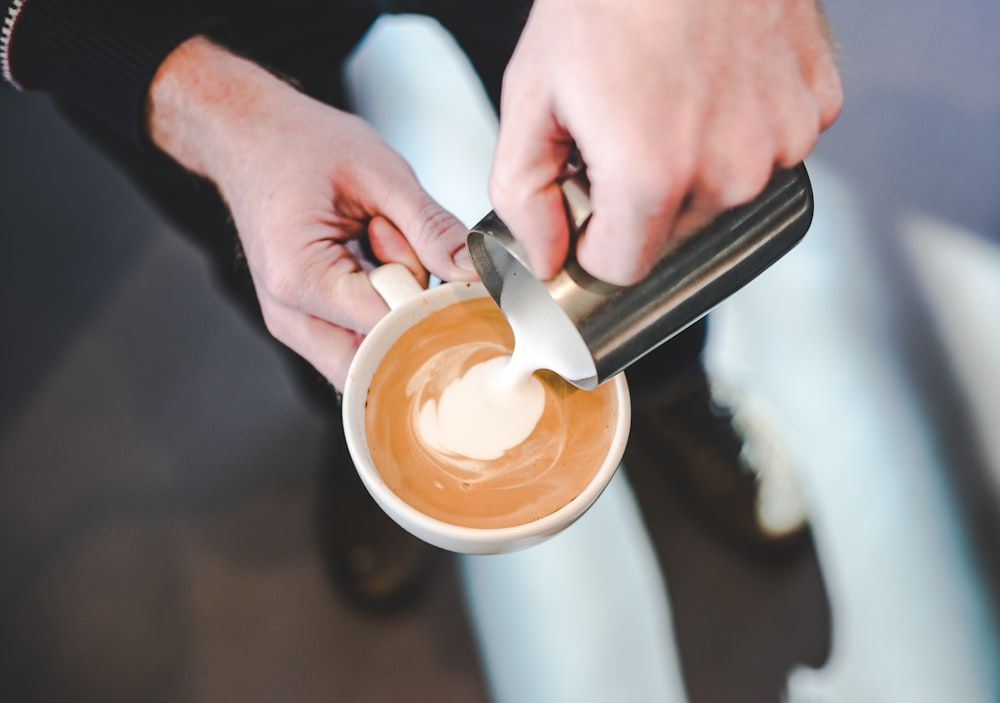 person pouring milk in coffe