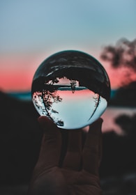 A peaceful hand holding a glowing crystal ball against a twilight sky.