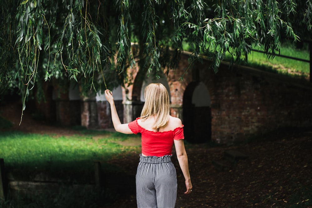 woman standing grabbing green tree leaf wearing red t-shirt