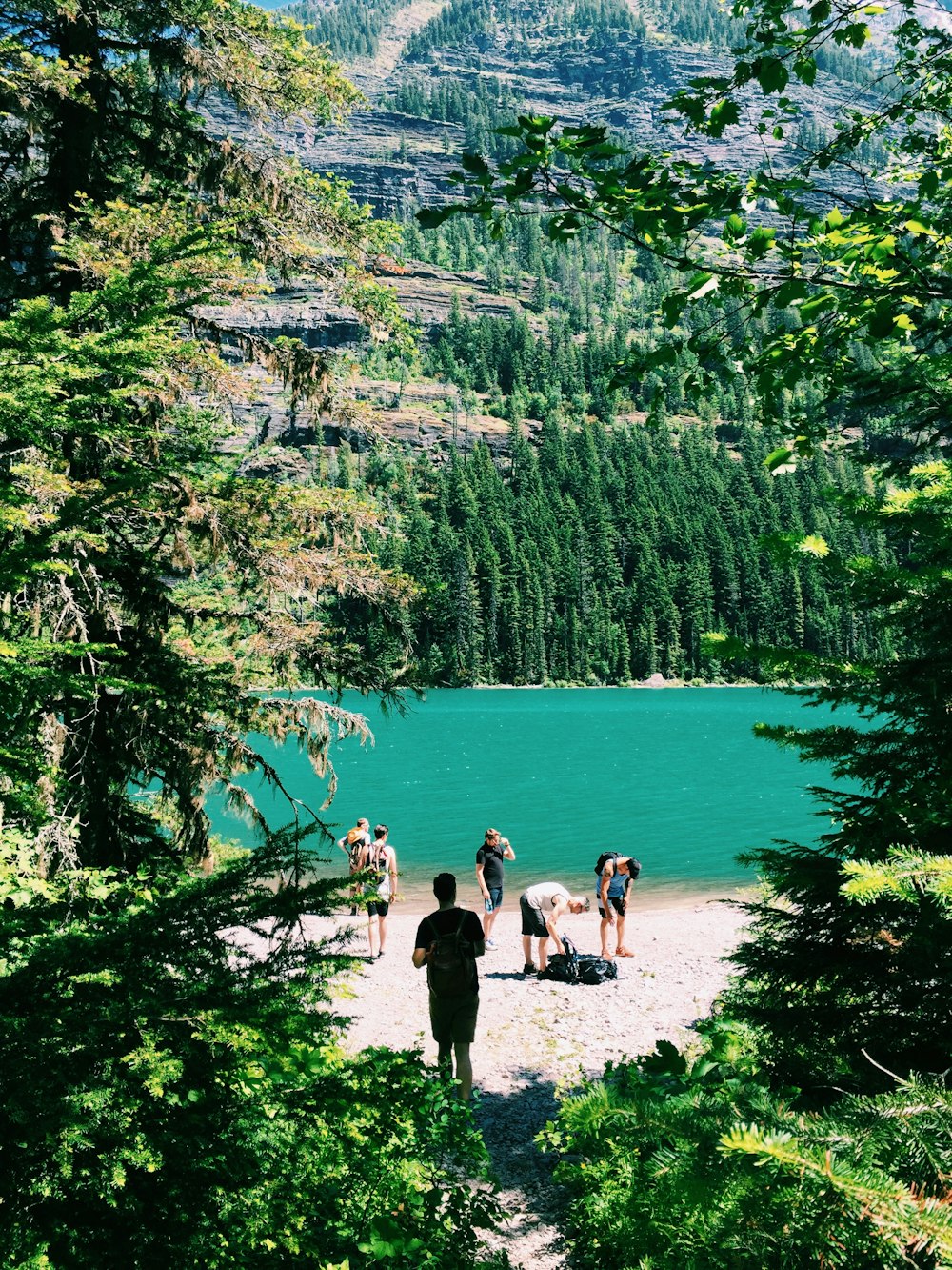 grupo de pessoas em pé ao lado de árvores e lago perto da montanha
