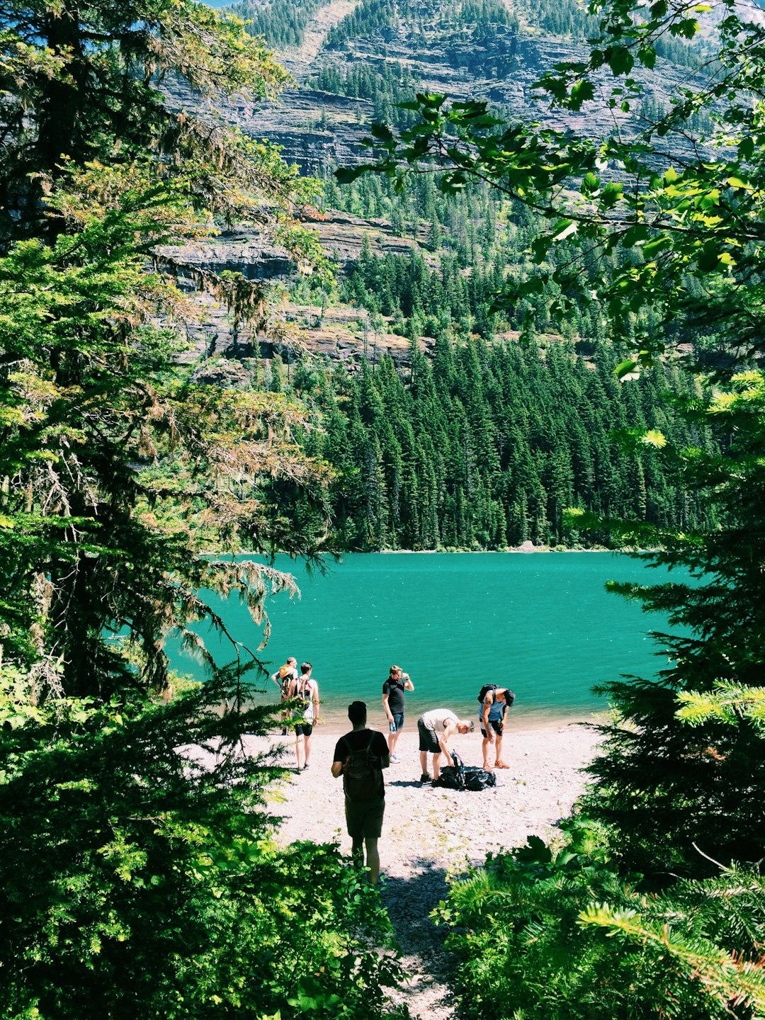 group of people standing beside trees and lake near mountain