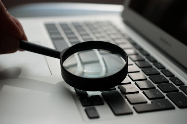 A magnifying glass hovering over a suspicious website on a laptop screen.