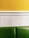 A minimalist interior wall design featuring a yellow upper section, a white beadboard midsection, and a green cushioned bench at the bottom.