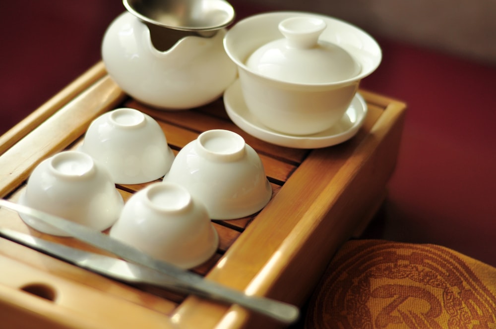 four white ceramic bowls near teapot and tureen on brown wooden tray