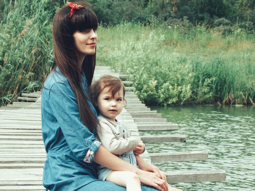 woman holding her child on dock near body of water