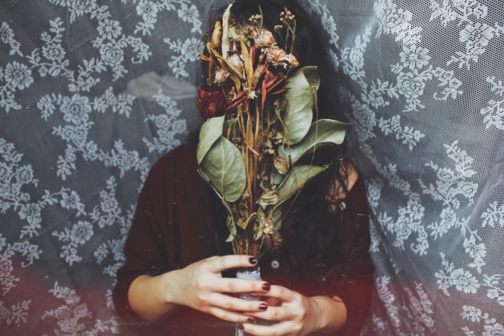 person holding green and red flower bouquet standing against floral background