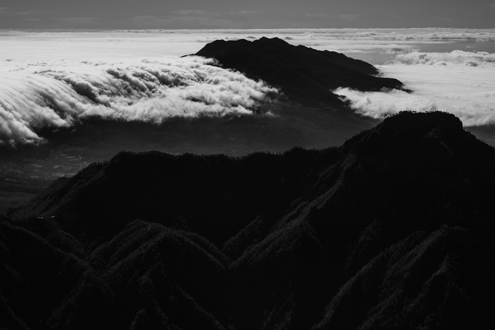 Graustufenfotografie von Bergen, die von Wolken bedeckt sind