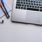 silver laptop computer beside white ruled paper