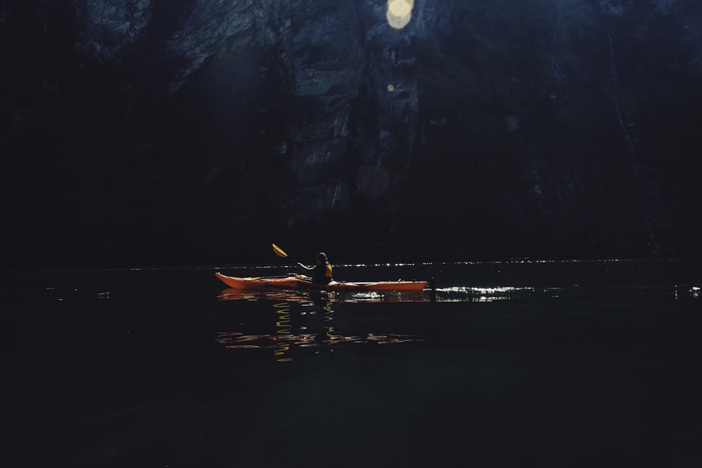 Persona montada en kayak rojo mientras rema en un cuerpo de agua