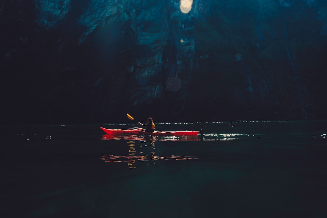 person riding on red kayak while paddling on body of water