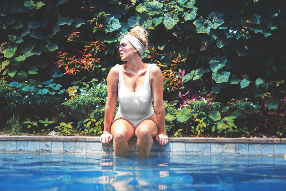 Frau im weißen einteiligen Bikini sitzt auf dem Pool