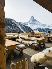 A rustic mountain restaurant with outdoor seating overlooking snowy peaks.