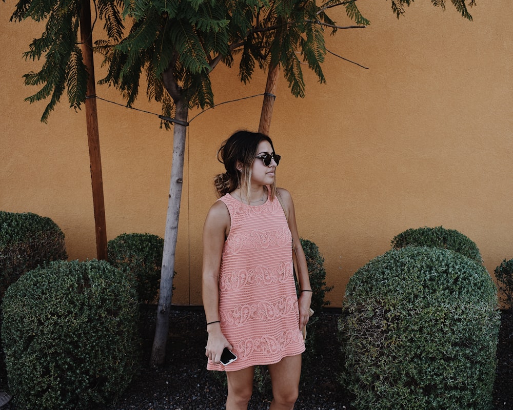 woman in pink sleeveless shift mini dress standing near bushes at daytime