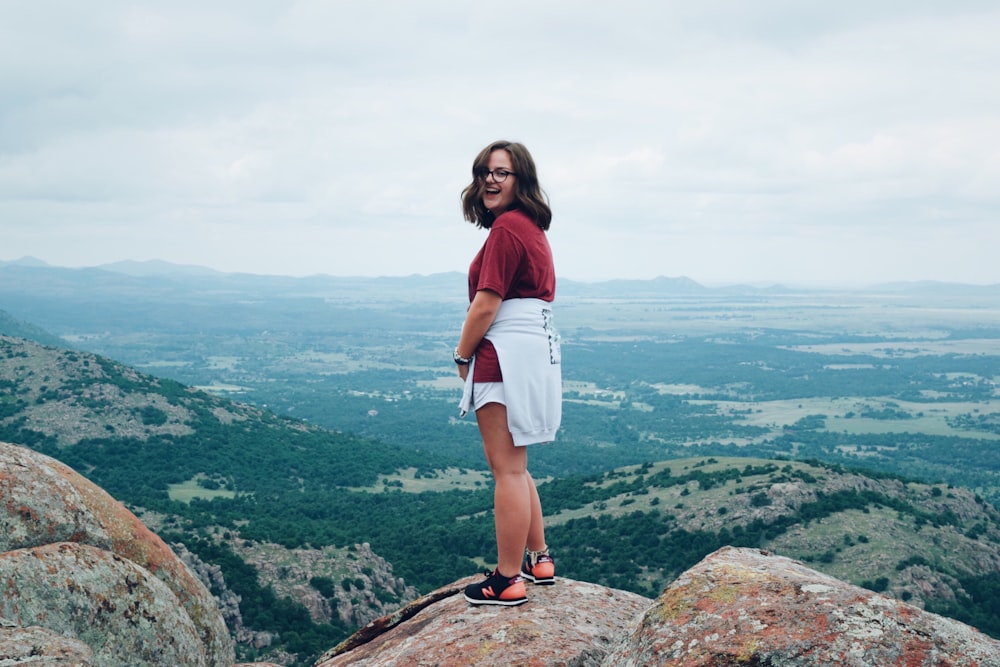 woman in red t-shirt standing on rock during daytime