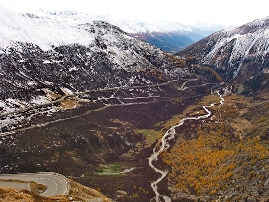 body of water between snow-capped mountains at daytime in Furka Pass Switzerland