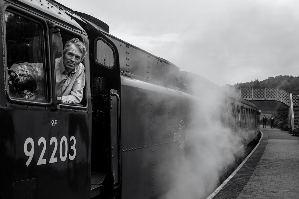 grayscale photography of man riding train