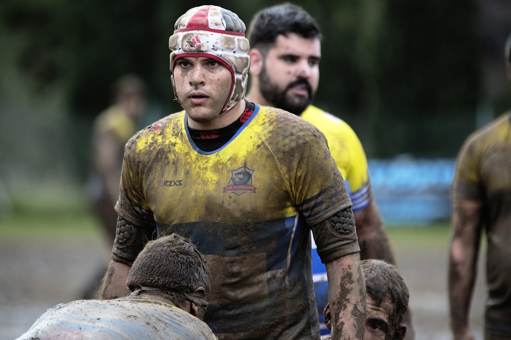 man wearing yellow and blue shirt on mud field during daytime