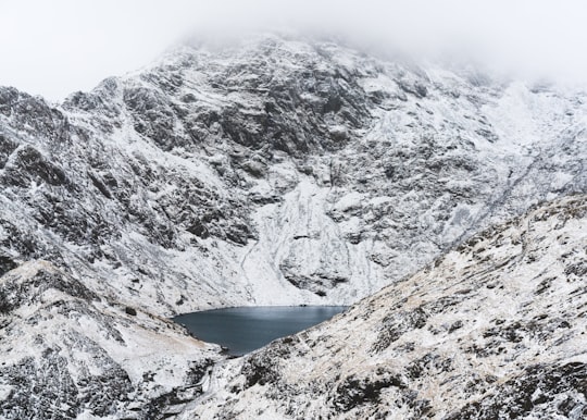 calm body of water surrounded with snow capped mountain at daytime in Snowdon United Kingdom