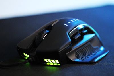A sleek, black gaming mouse featuring a textured grip, multiple side buttons, and illuminated areas emitting green light. The mouse has a robust and ergonomic design, with a scroll wheel and other controls positioned for easy access.