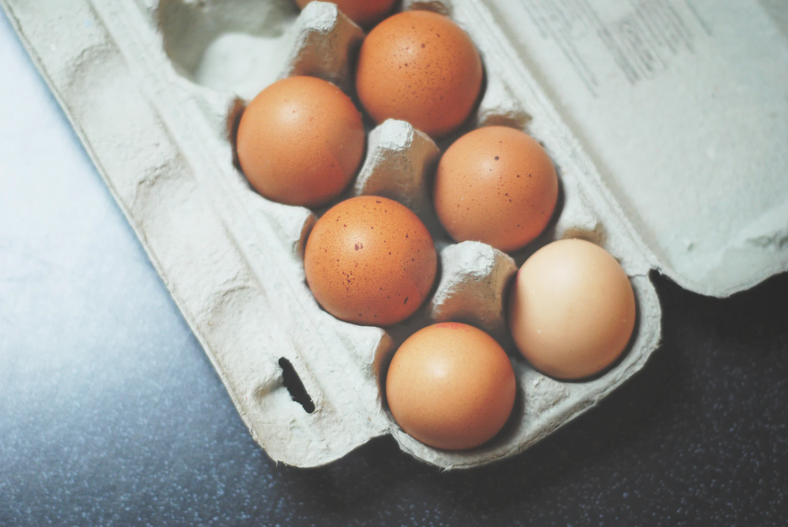 Brown eggs sitting in an open pulp carton on a dark kitchen worktop
