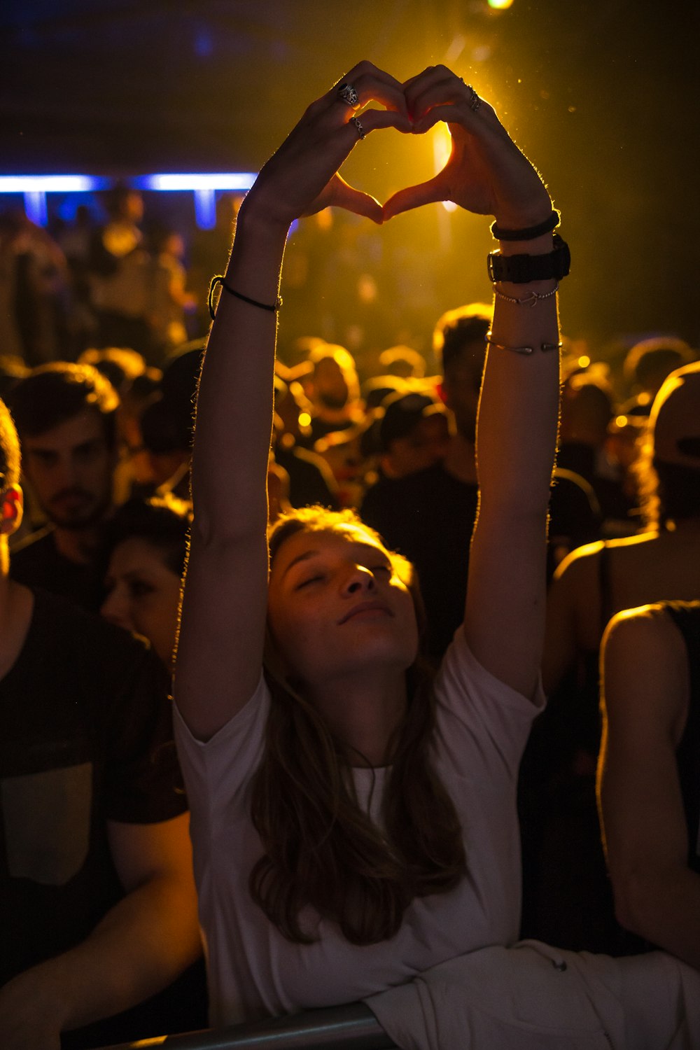 Mujer en la multitud levantando la mano mientras hace la señal del corazón