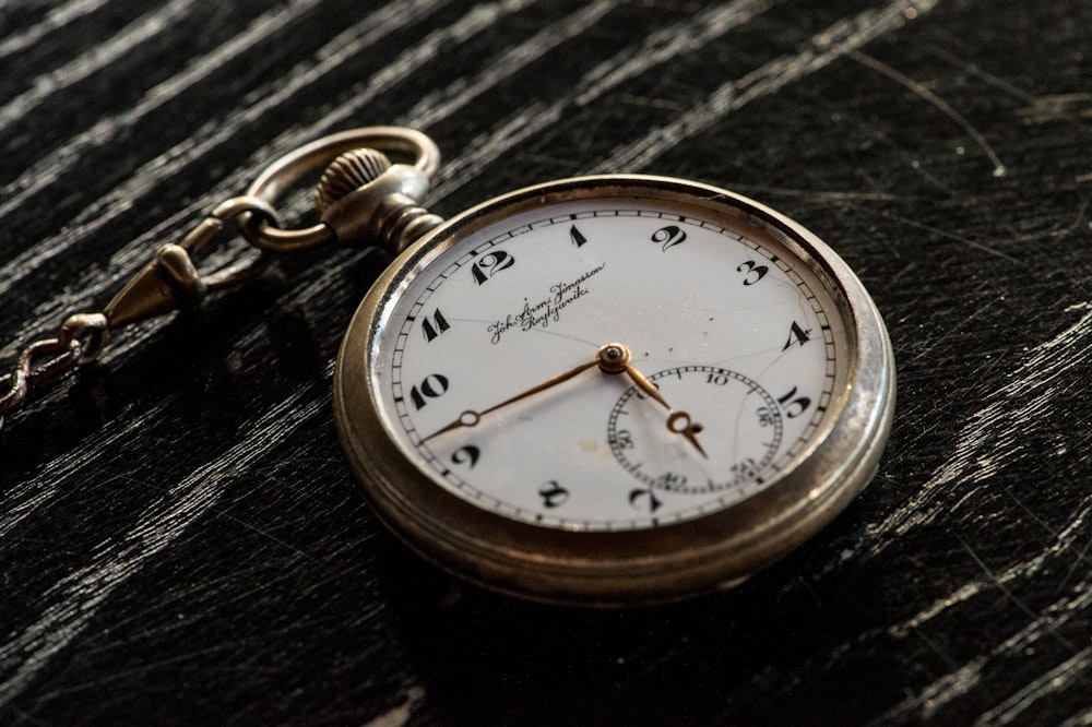 round silver-colored analog pocket watch on table