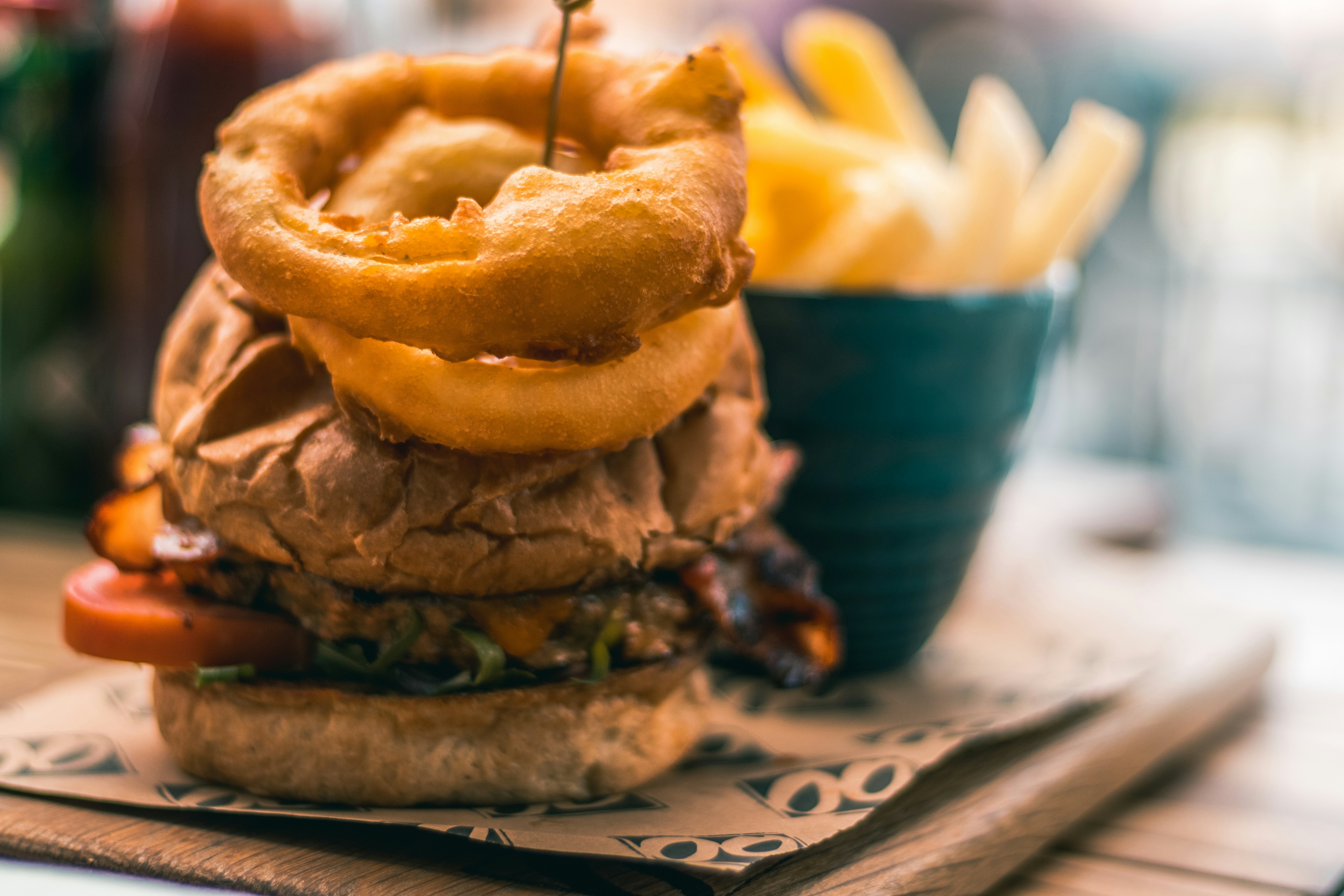 Tall burger topped with onion rings and fries on a wooden board