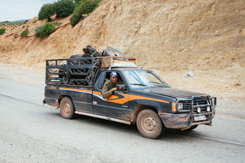 Black pickup truck towing a trailer carrying compact construction equipment on a rural road.