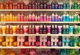 A well-organized display of colorful cosmetic or bath products arranged on multiple shelves. The bottles and boxes are in an array of colors including orange, pink, purple, blue, and green, each with unique product labeling. The arrangement creates a visually appealing rainbow effect.