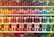 A well-organized display of colorful cosmetic or bath products arranged on multiple shelves. The bottles and boxes are in an array of colors including orange, pink, purple, blue, and green, each with unique product labeling. The arrangement creates a visually appealing rainbow effect.