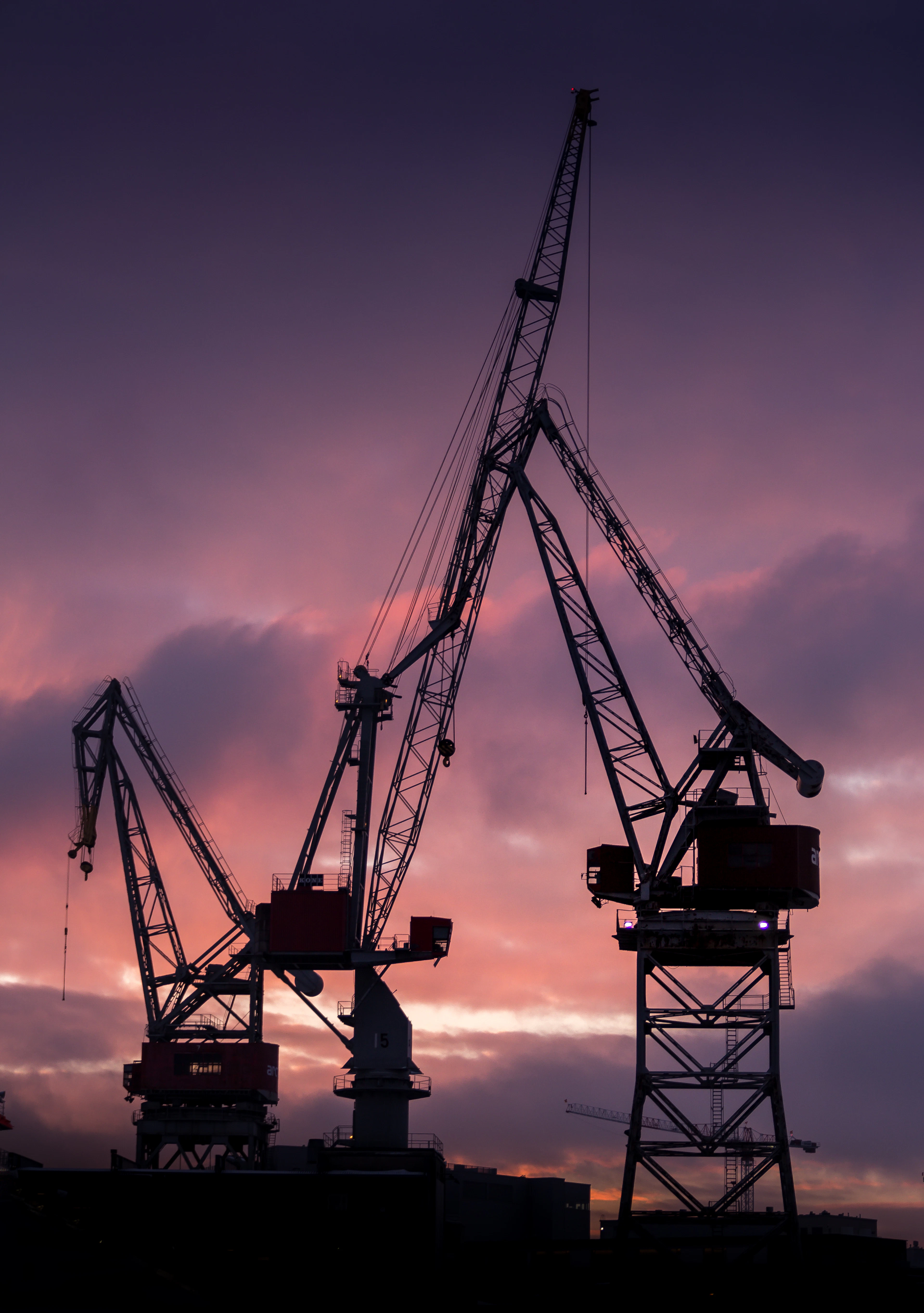 Gantry cranes silhouetted against a violet dusk sky at a container terminal.