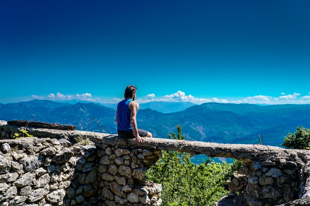 man sitting on gray concrete cliff