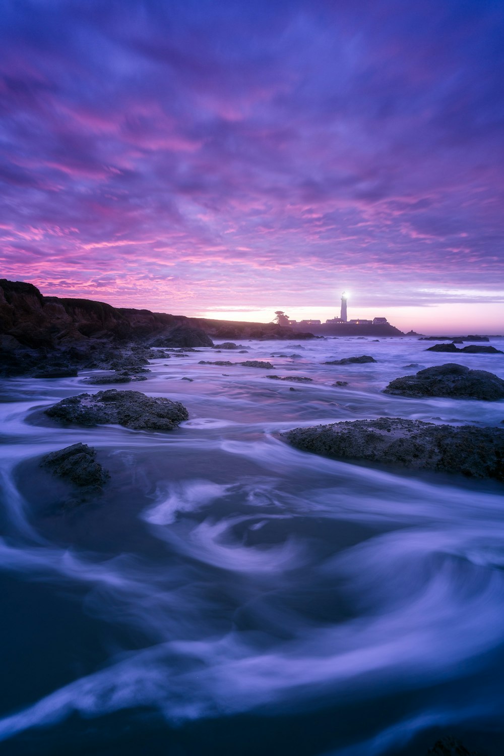 rocks and sea with silhouette of lighthouse in background