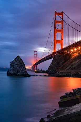 A golden hour shot of the San Francisco Bay Bridge shimmering against a moody twilight sky.