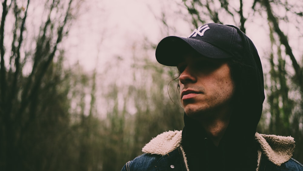 selective focus of man wearing black and white fitted cap in forest at daytime